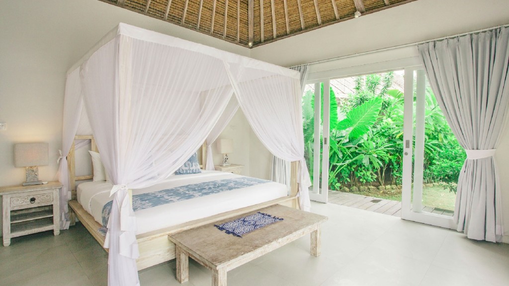 Escape to a tropical white bedroom with curtains and earth color ceiling thatch roof showing garden on the exterior